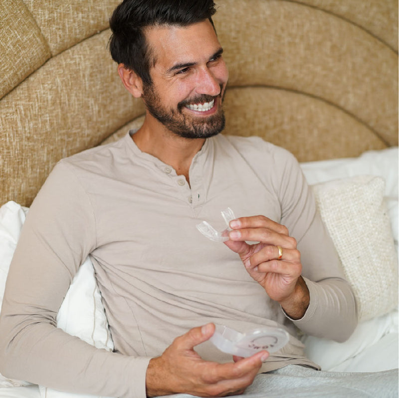 Man in bed holding a nightguard